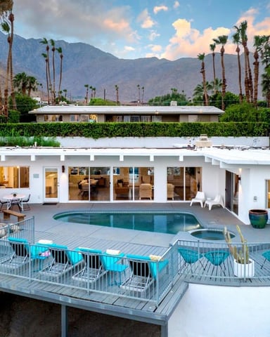 Modern white mid-century home with pool, palm trees, and mountain backdrop at sunset