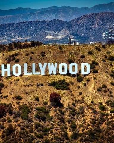Hollywood sign on dry hillside with mountains and communication tower in background