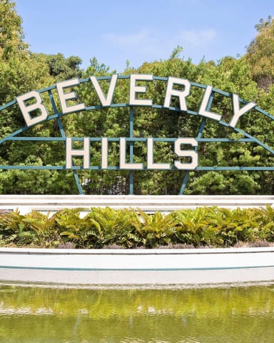 Beverly Hills arched sign with blue metal frame and white letters over landscaped planter and pond