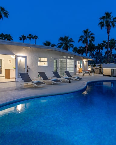 Modern white house with pool, lounge chairs, and palm trees at dusk