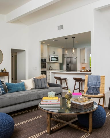 Open-plan living room with gray sofa, round coffee table, and kitchen with stainless steel appliances visible through opening