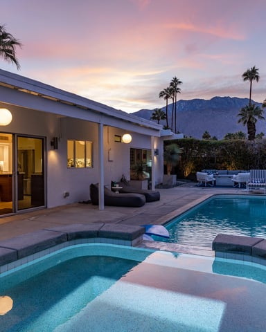 Mid-century modern house with pool and spa at dusk, palm trees and mountains visible beyond