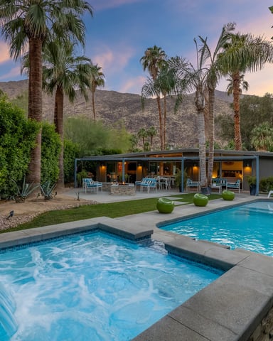 Backyard with spa and swimming pool, modern house, palm trees, and desert mountains at sunset