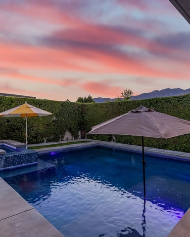 Backyard pool with spa, umbrellas, and mountain views at sunset with pink sky