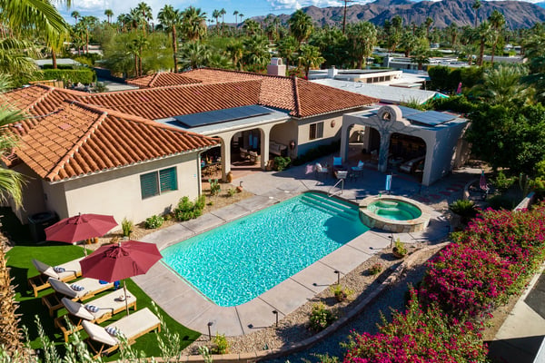 Desert home with turquoise pool, spa, red umbrellas, and mountain views surrounded by palm trees