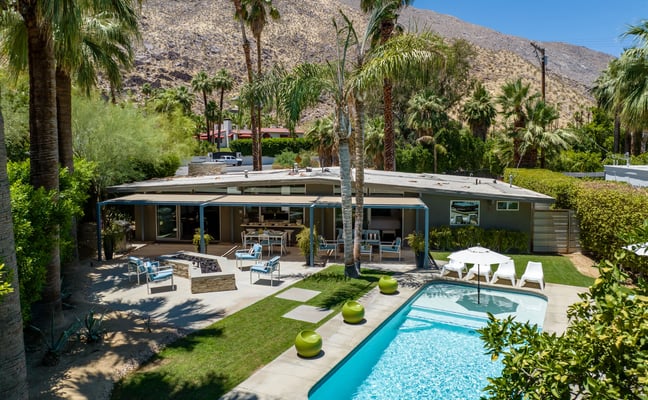 Mid-century modern house with pool, patio, and palm trees against desert mountain backdrop